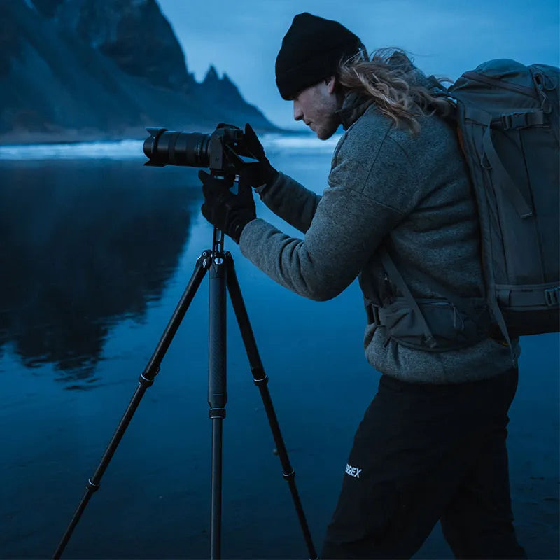 The TreeRoot in real field use — a photographer shooting low-light beach landscapes, showing the twist-lock carbon legs at a working height